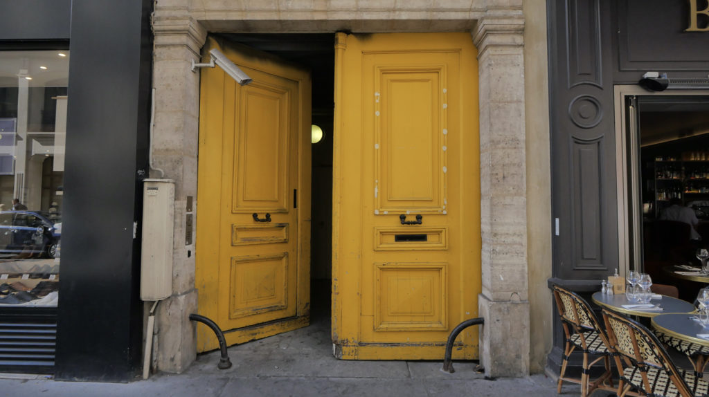 Porte jaune d'un immeuble parisien ouverte avec une caméra de vidéosurveillance filmant l'entrée